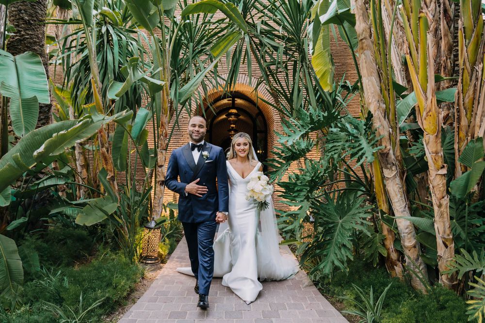 A couple walks down a tropical garden path lined with lush banana trees and palms.
