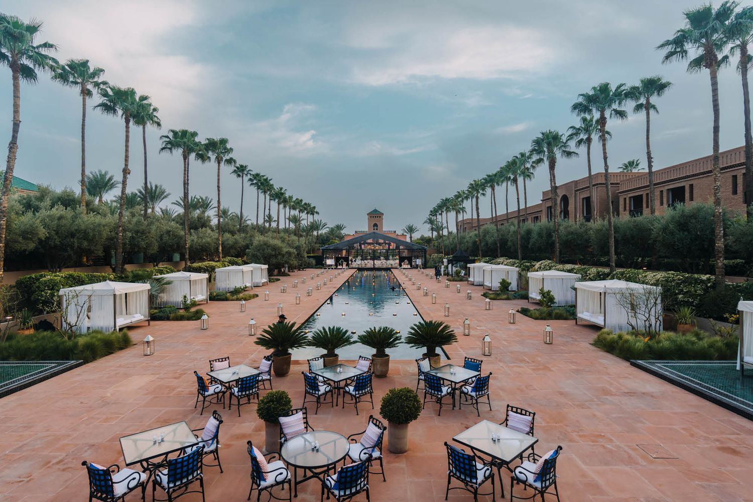 A symmetrical outdoor venue setup with palm trees lining a reflecting pool and tables arranged for an event.