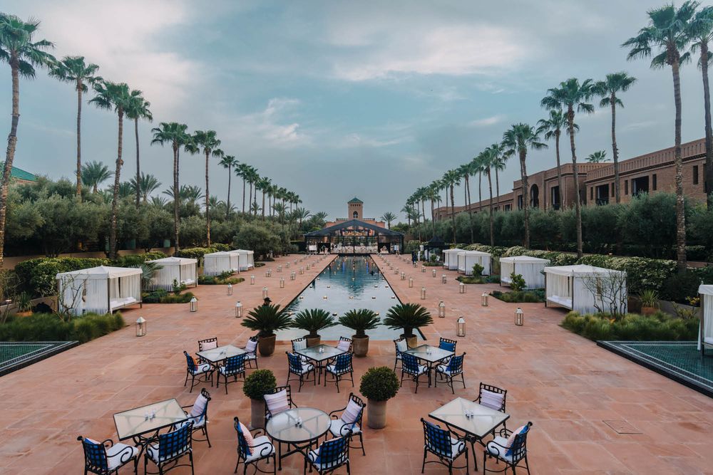A symmetrical outdoor venue setup with palm trees lining a reflecting pool and tables arranged for an event.