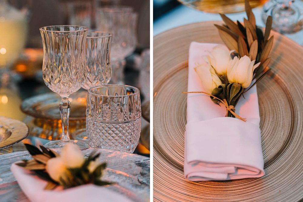 Close-up of elegant table settings with crystal glasses and pink napkins decorated with feathers and leaves.