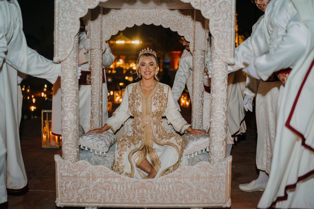 Ornate white and gold decorated wedding carriage illuminated by warm lighting during an evening celebration.