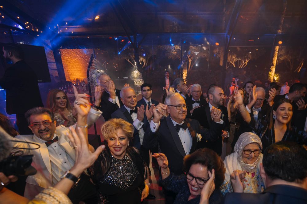 A crowded room of party attendees cheering and raising their hands during a celebratory event with blue lighting.
