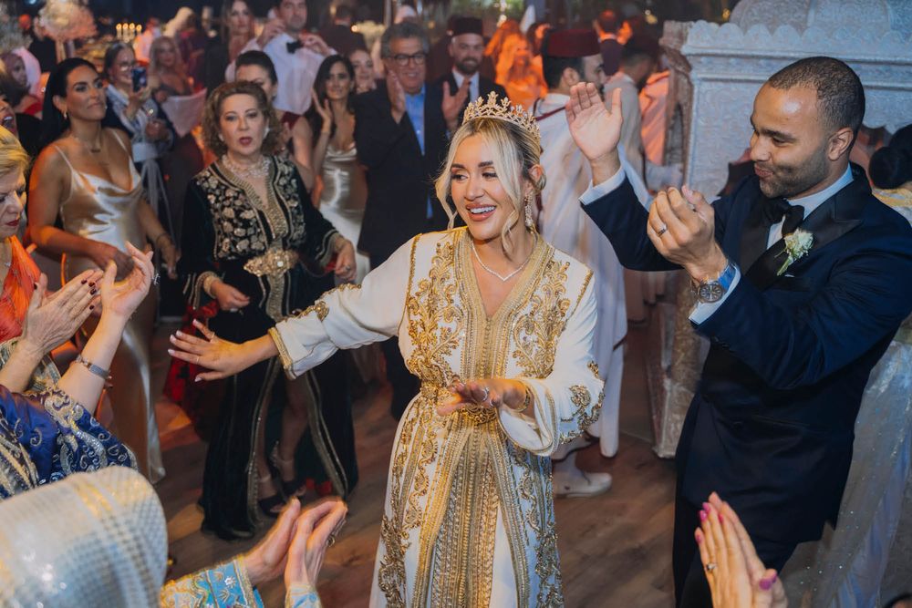 Wedding guests dancing and celebrating on a dance floor as a couple in festive attire leads the party atmosphere.