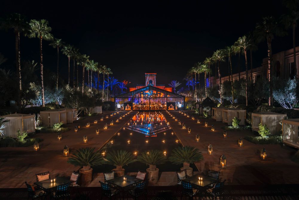 Palm tree-lined pathway illuminated with lanterns leading to a glowing building facade with blue lighting.