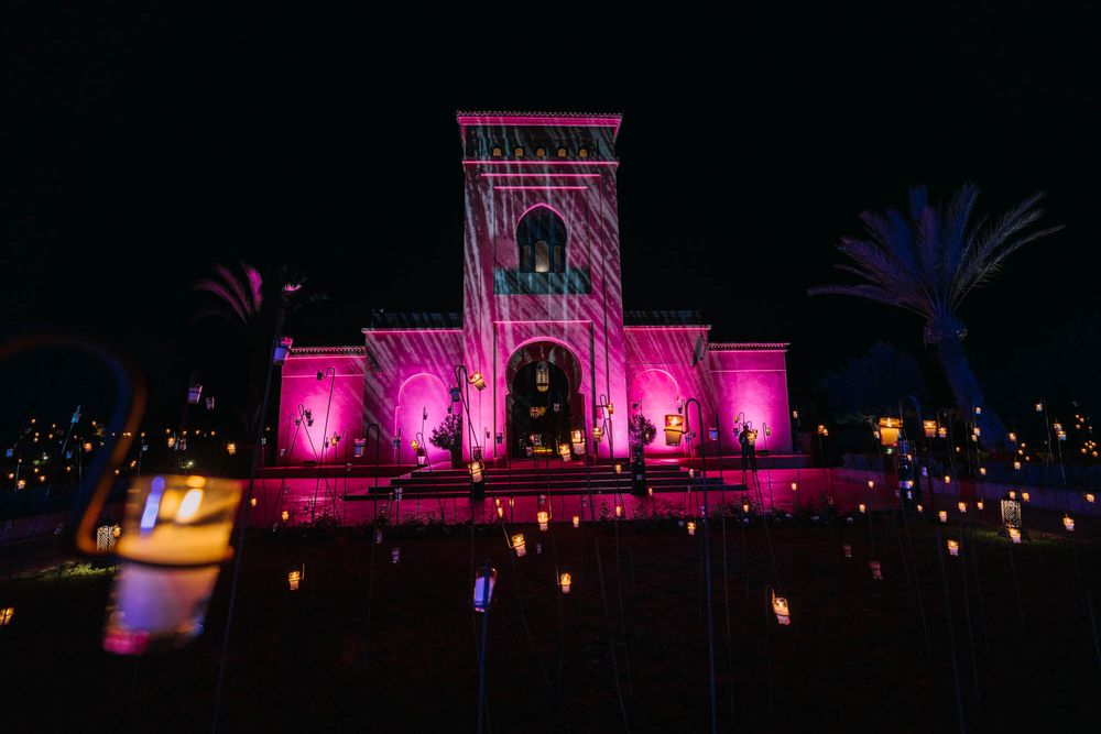 Historic building facade illuminated in vibrant pink lighting with palm trees and ground lights creating ambiance.