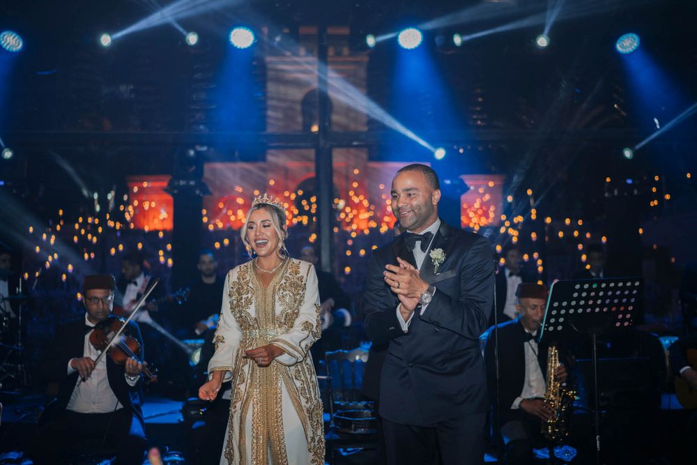 Performers stand on stage during an evening concert with dramatic blue lighting and glowing decorative lights in background.