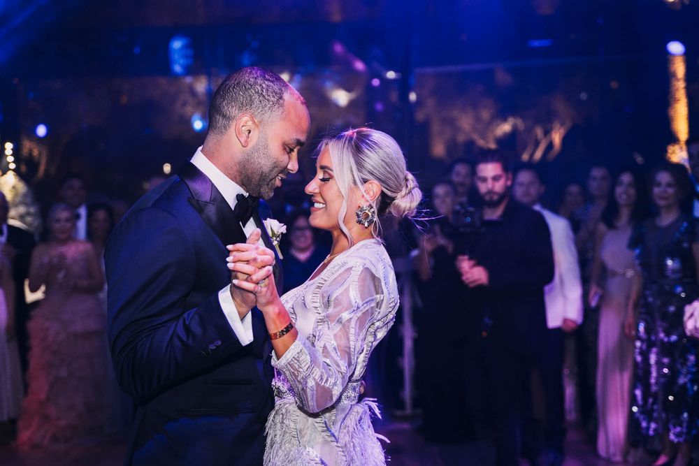 A couple shares their first dance together at their wedding reception in a dimly lit venue with blue lighting.