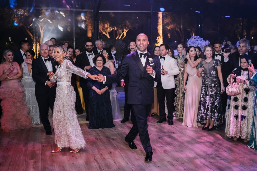 Wedding guests and attendees dance together on a pink-lit dance floor during an elegant evening celebration.