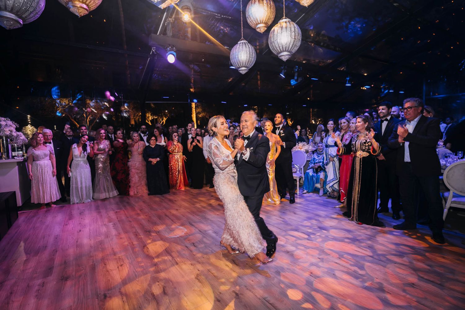 A dance floor ablaze with atmospheric lighting and paper lanterns while a couple shares their first dance at a wedding reception.