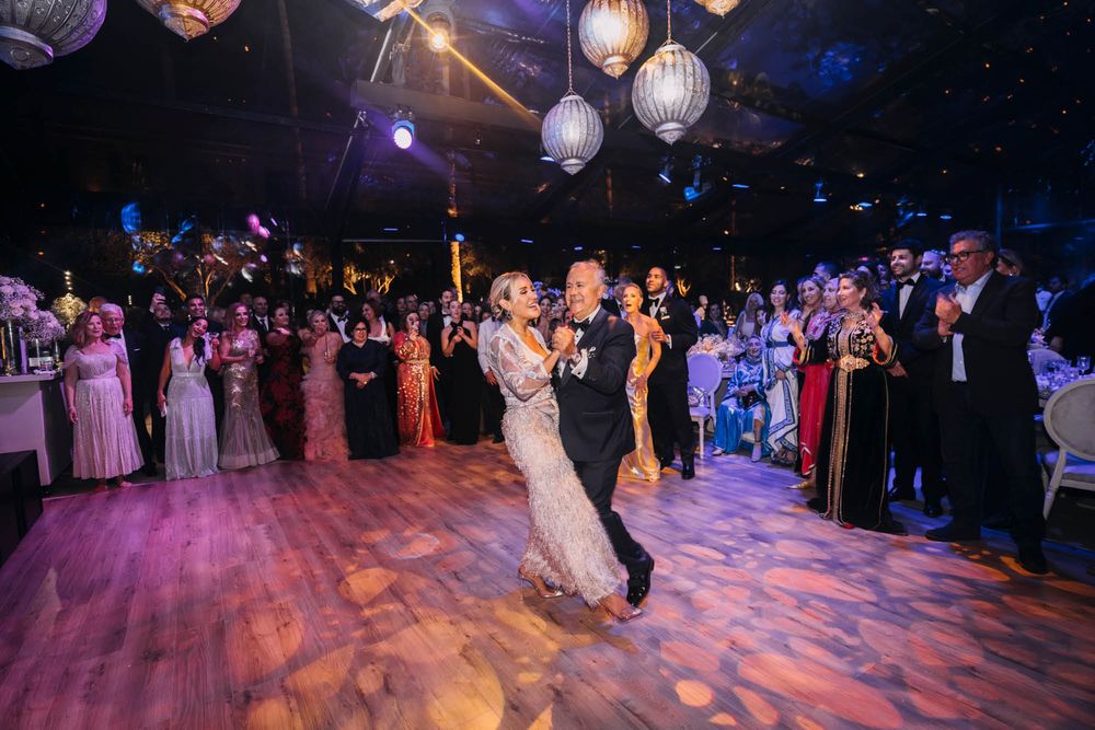 A dance floor ablaze with atmospheric lighting and paper lanterns while a couple shares their first dance at a wedding reception.