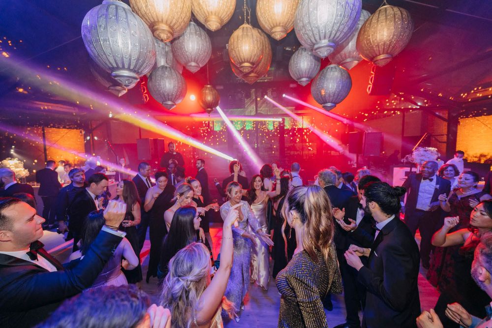 Crowded nightclub dance floor with hanging lantern decorations illuminated by red and white spotlights.