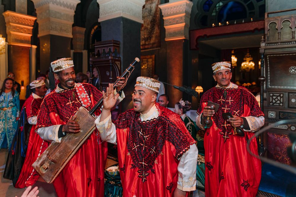 Musicians in vibrant red traditional costumes perform with medieval instruments at an ornate indoor venue.