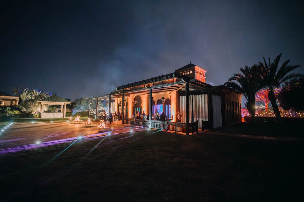 Nighttime view of an illuminated event venue with palm trees and colorful lighting creating a dramatic atmosphere.