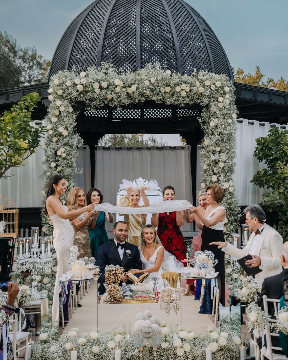 A celebration in an elegant garden gazebo decorated with white floral arrangements and crystal glassware.