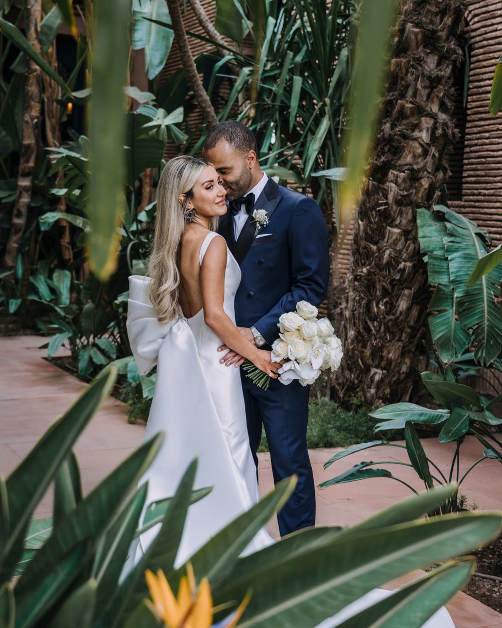 Couple embraces in a lush tropical garden setting with bamboo and palm trees surrounding them.