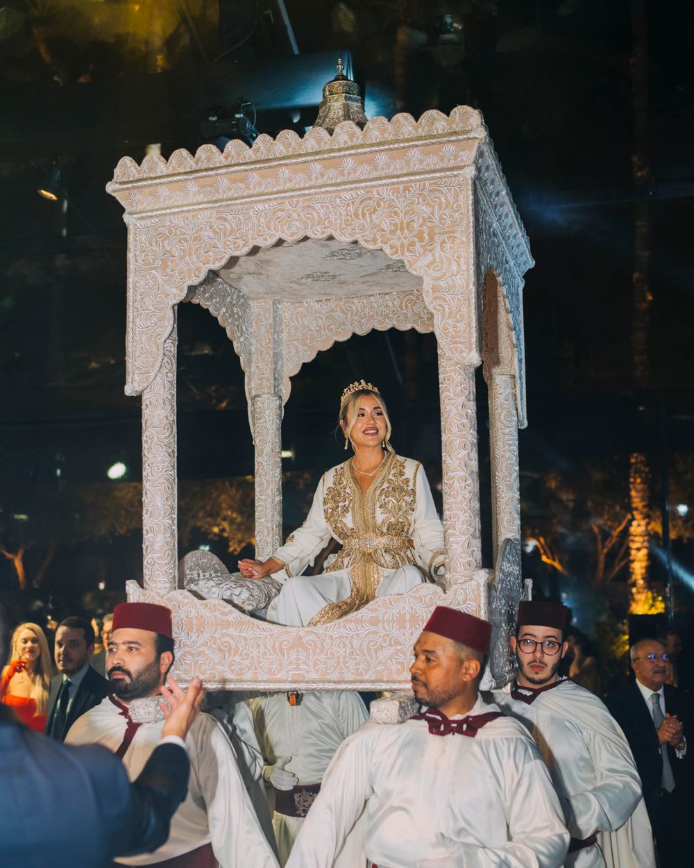 Traditional Moroccan wedding procession with an ornate white palanquin carried by men in traditional clothing.
