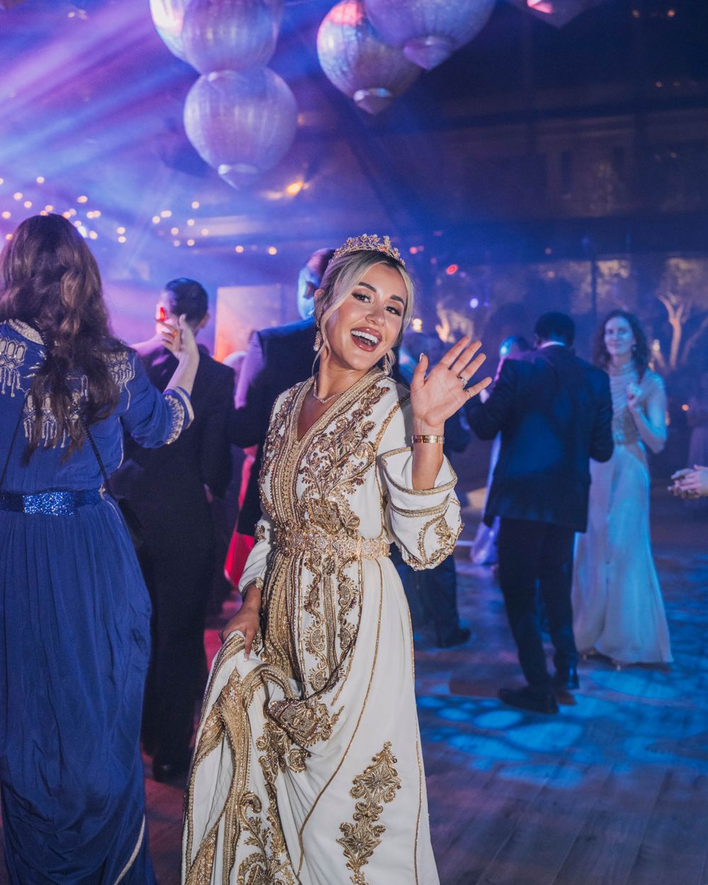 Party guests dancing under glowing purple lights and round white lanterns with elegant formal attire at an evening celebration.