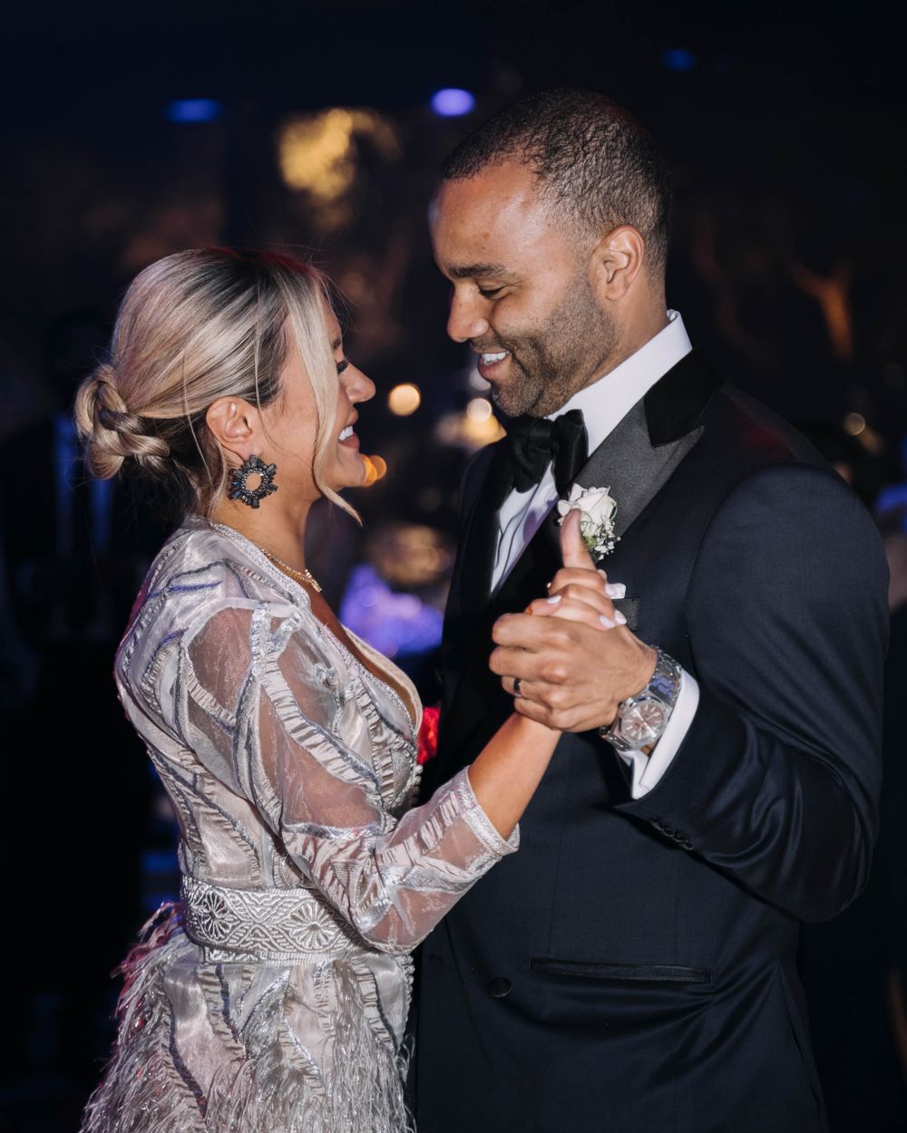A couple in formal attire sharing an intimate dance at an evening celebration with blurred lights in the background.