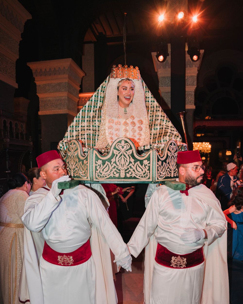 Traditional Moroccan wedding scene with attendants in white robes and red fez hats carrying a decorative wedding chair.