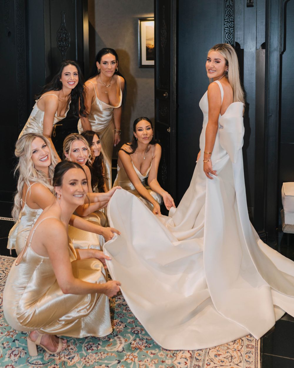 A wedding party gathers around a bride in a white satin gown, with bridesmaids wearing champagne silk dresses.
