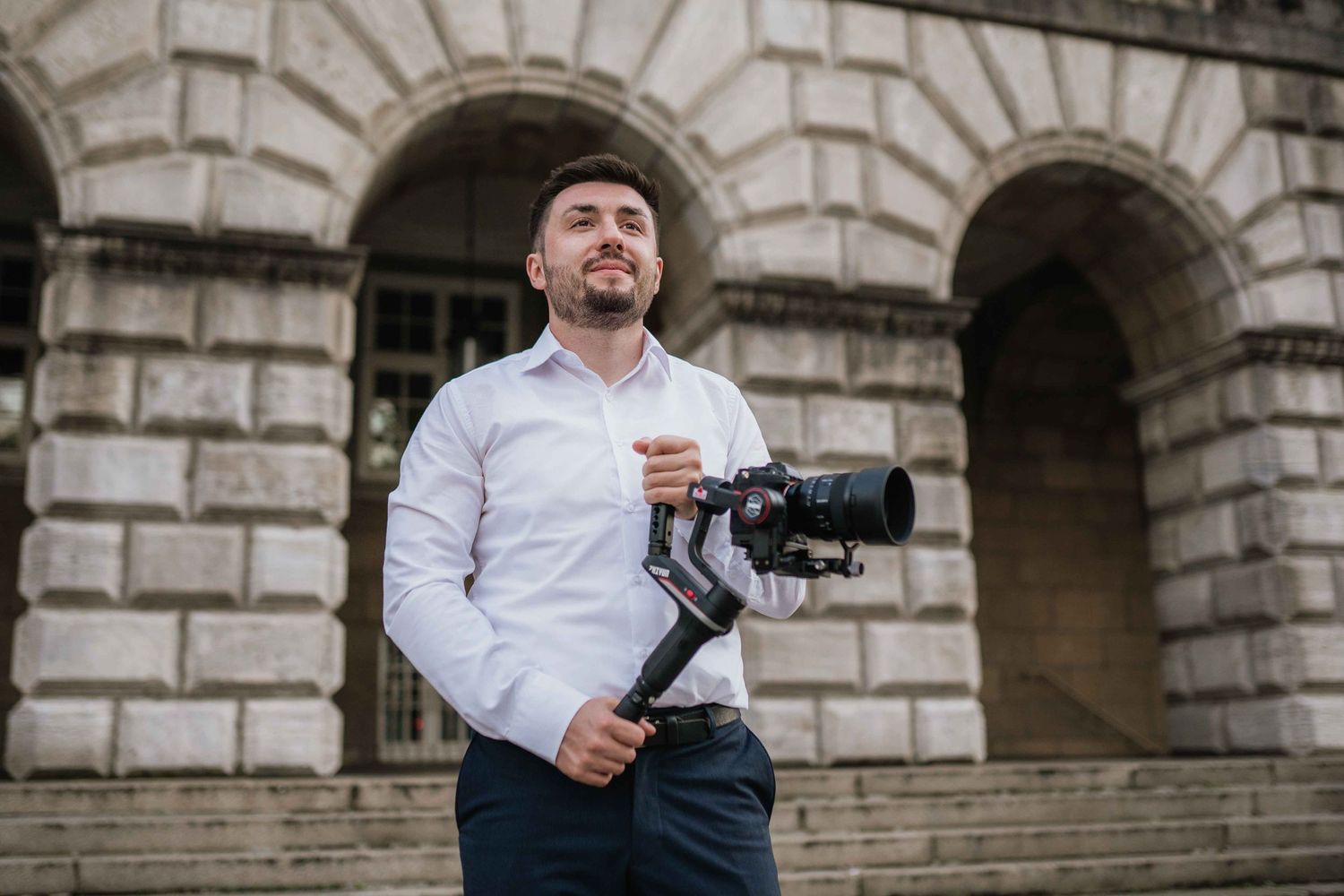 Wedding photographer with professional camera equipment against stone architecture.