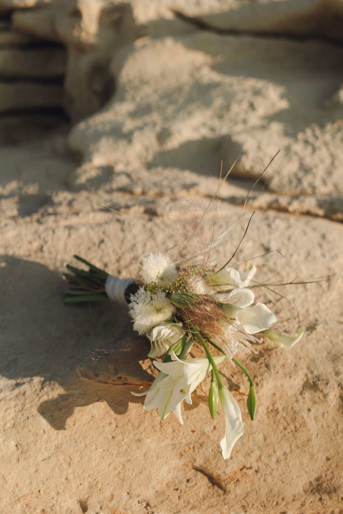 A delicate white floral bouquet lying on textured sandy ground.