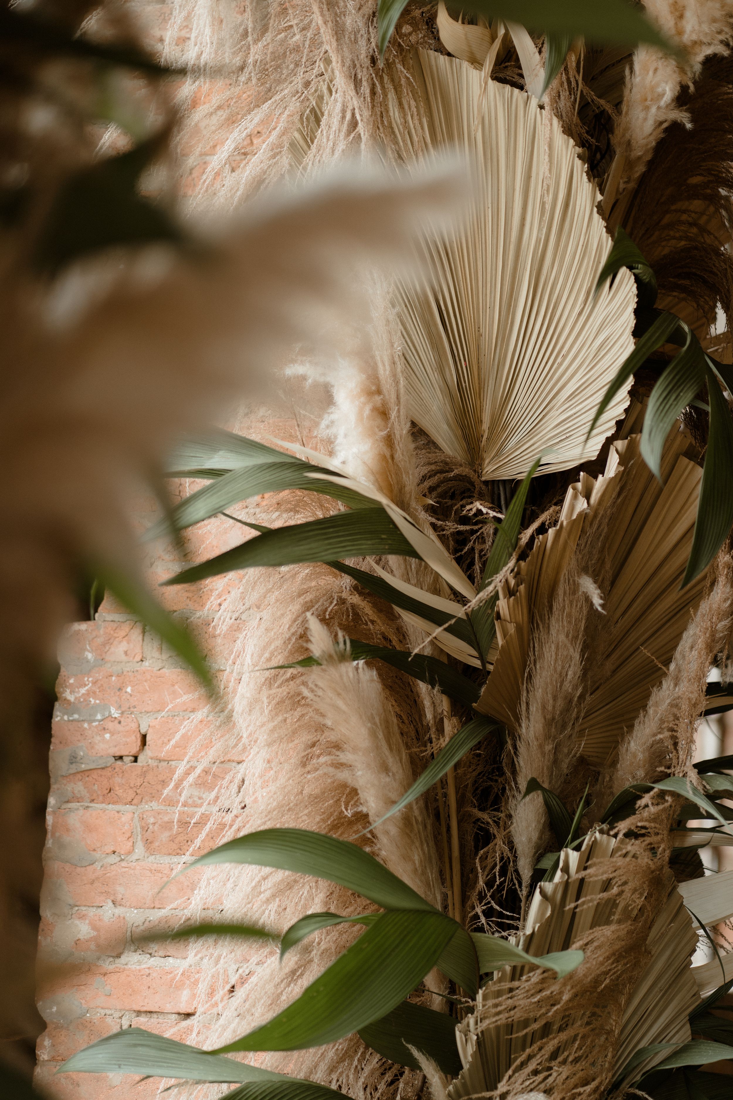 Dried palm fronds and foliage against exposed brick creating bohemian wedding decor.