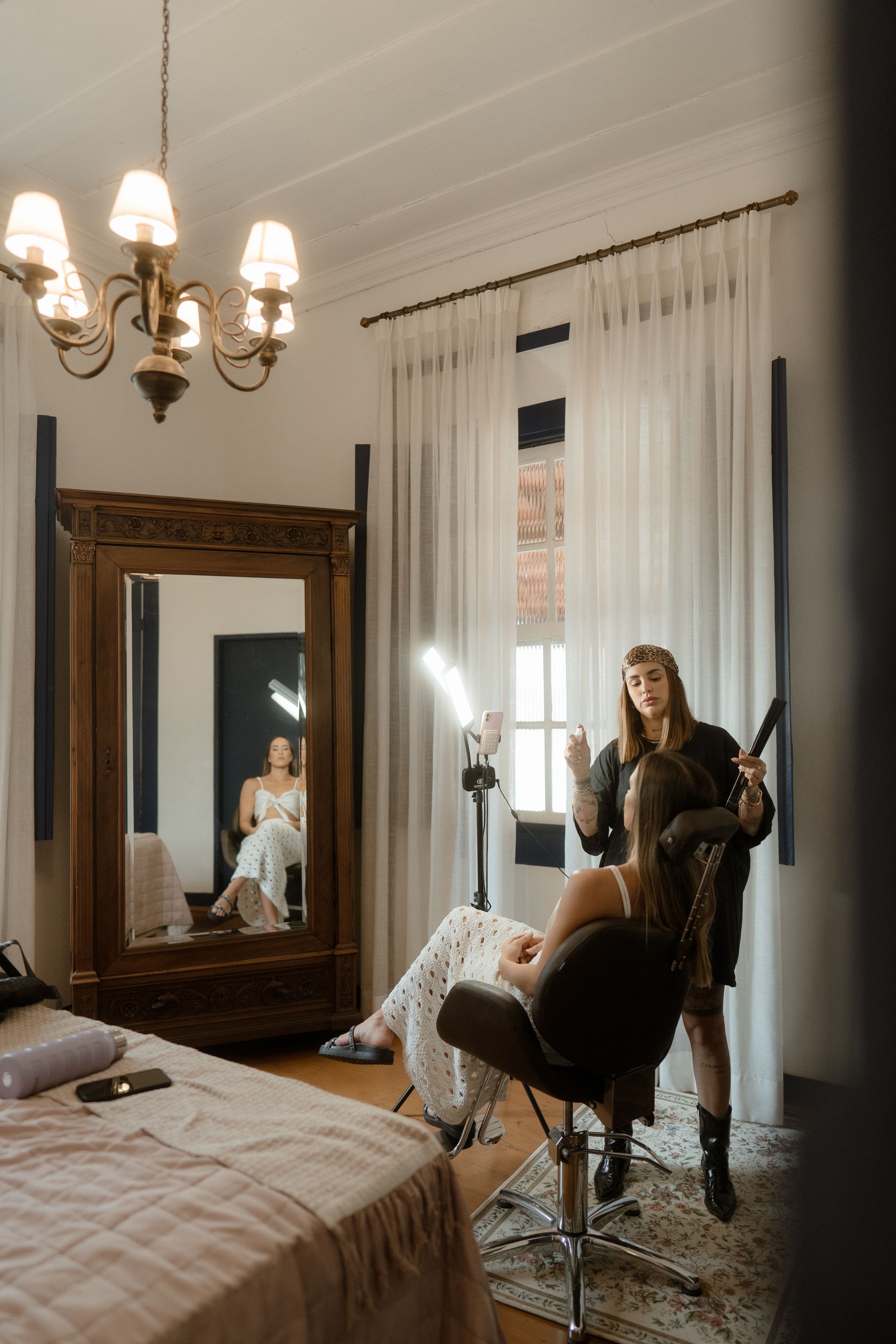 A cozy bedroom interior with sheer curtains and an ornate chandelier casting warm light.