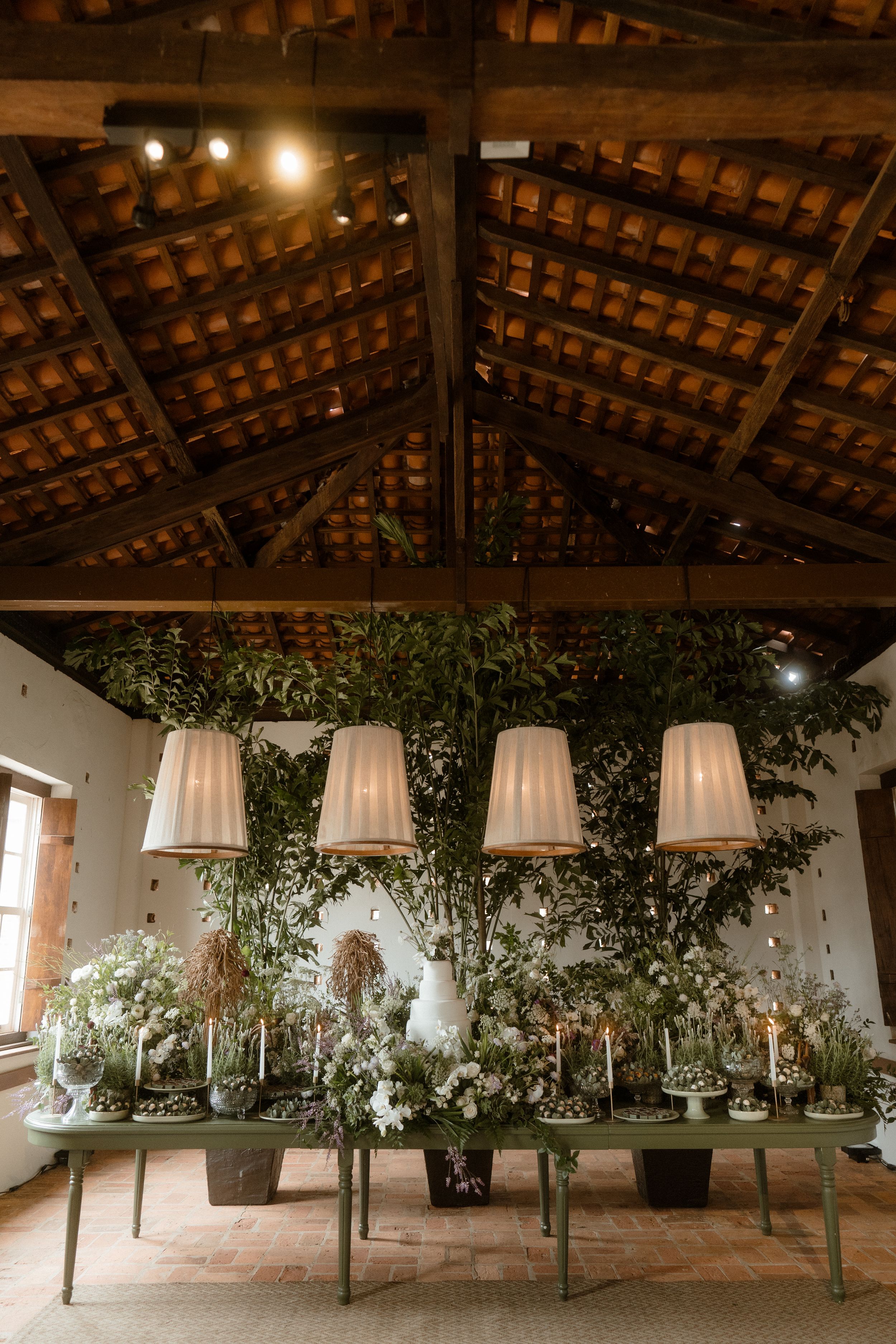 Industrial venue space with exposed wooden beam ceiling decorated with hanging greenery and drapes.