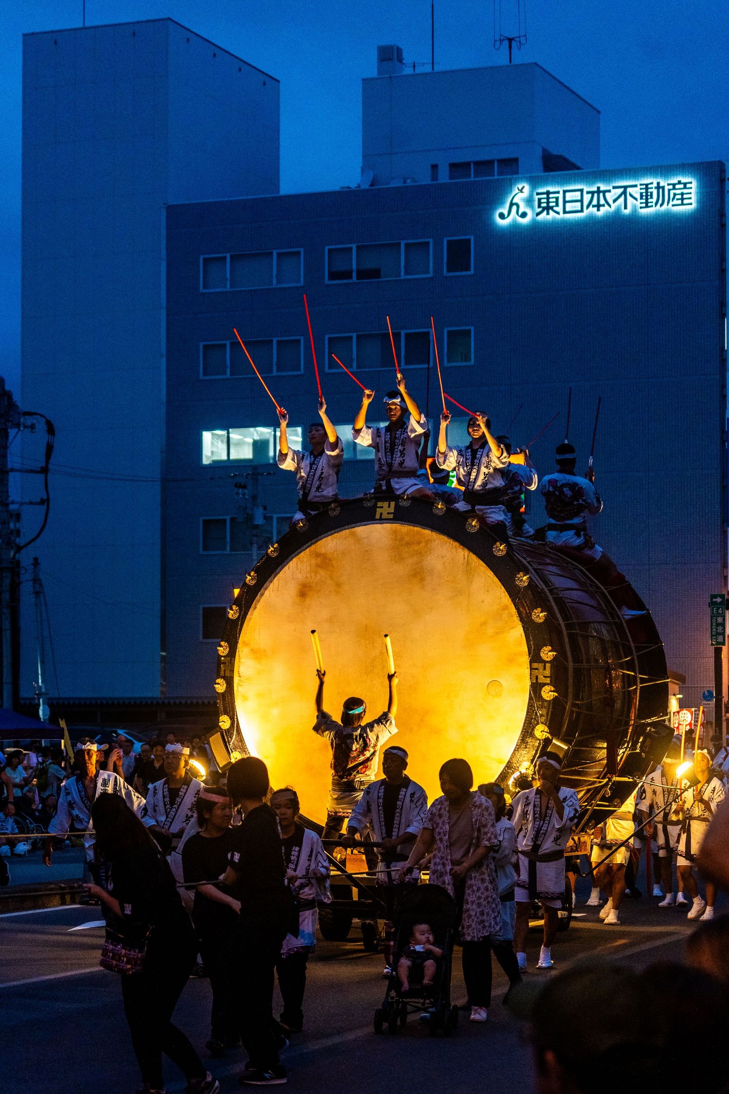 Japanese festival performers silhouetted against large illuminated drum at night.
