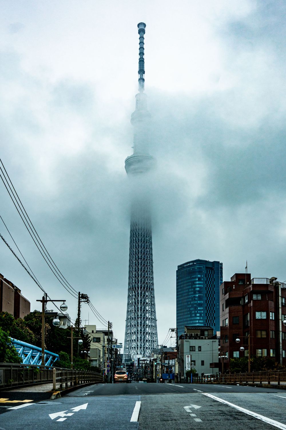 Tokyo Skytree tower disappearing into misty clouds on a gray day.