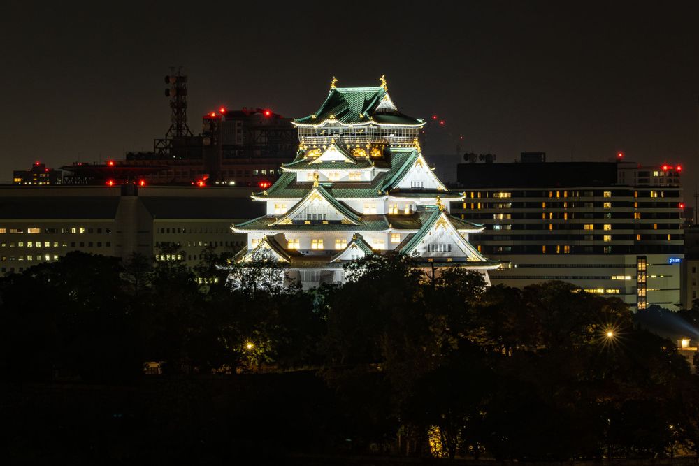 Illuminated Osaka Castle glowing against the night sky with city lights in the background.