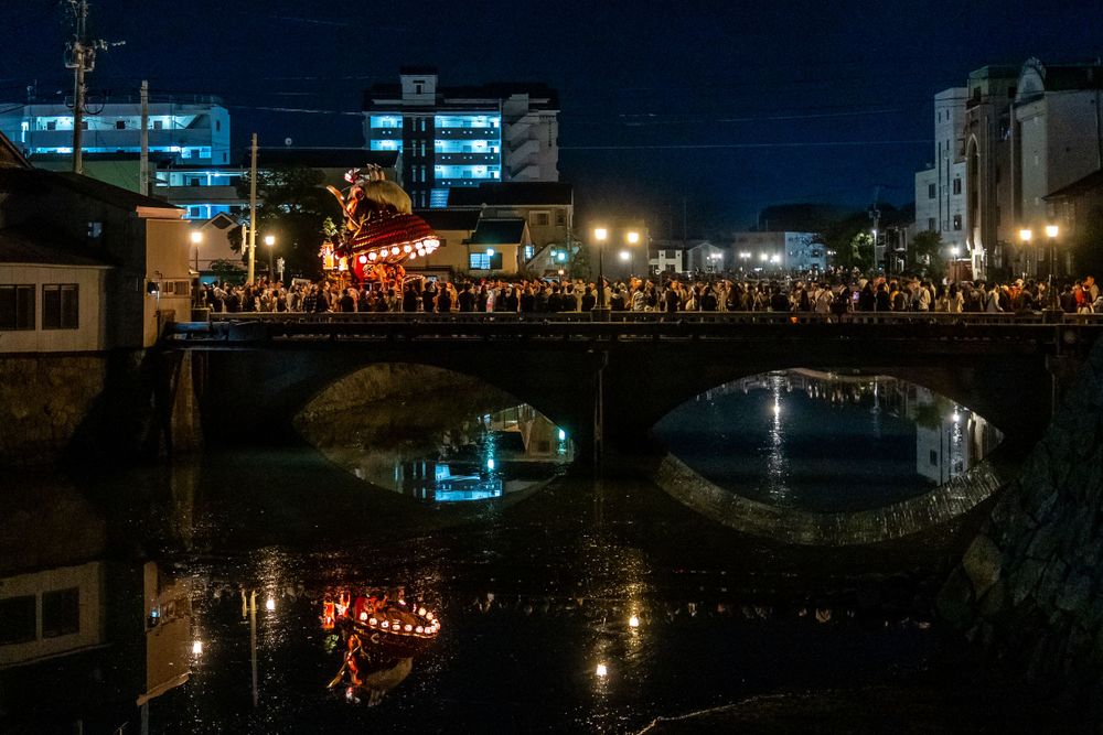 Traditional Japanese festival with lanterns reflecting over a canal at night.