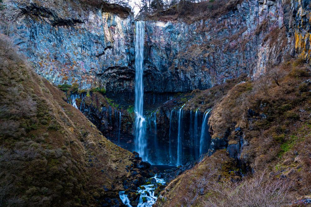 Dramatic blue-tinted waterfall flowing down rocky cliffs in winter landscape.