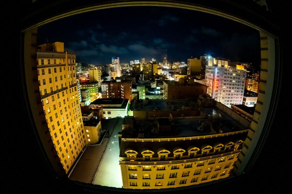 Fisheye view of illuminated city buildings at night creating curved architectural perspective.
