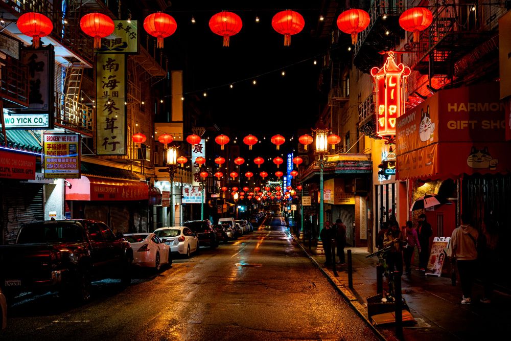 Red lanterns hanging over Chinatown street at night with neon signs.