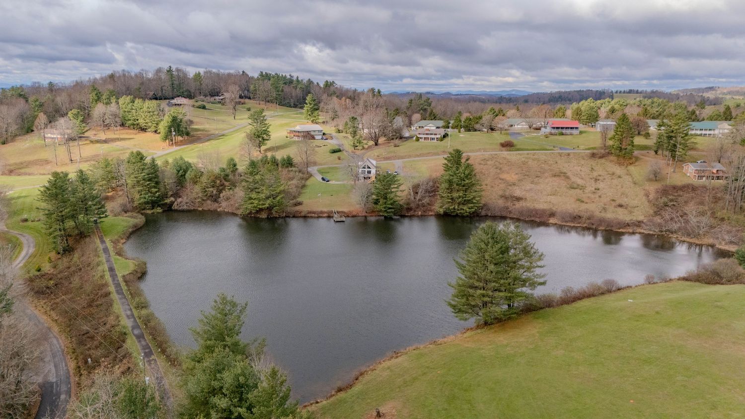 Scenic aerial view of a peaceful pond surrounded by rolling hills and scattered trees in autumn.