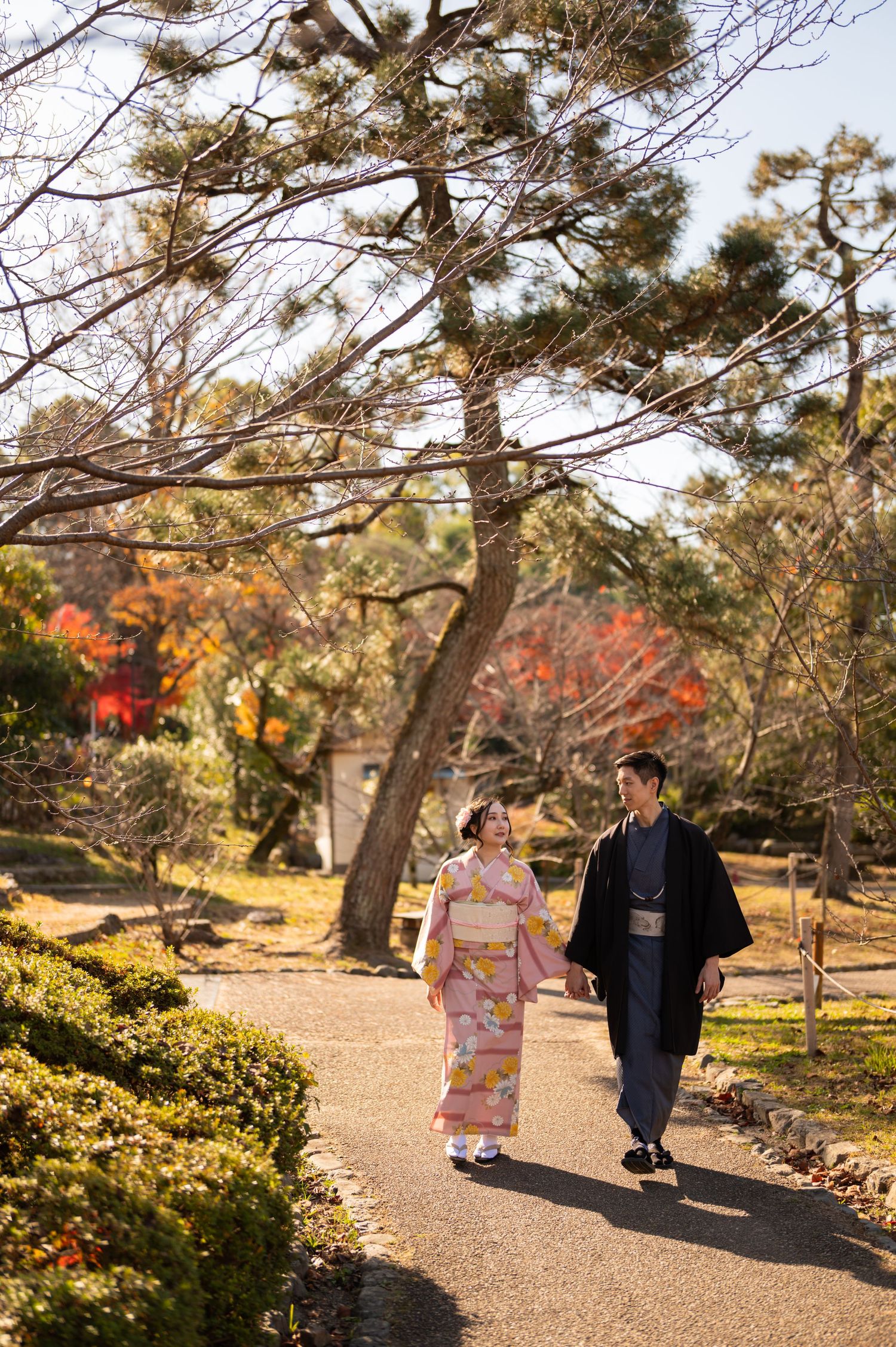 Couple in traditional Japanese kimono walking hand-in-hand through a scenic autumn garden.
