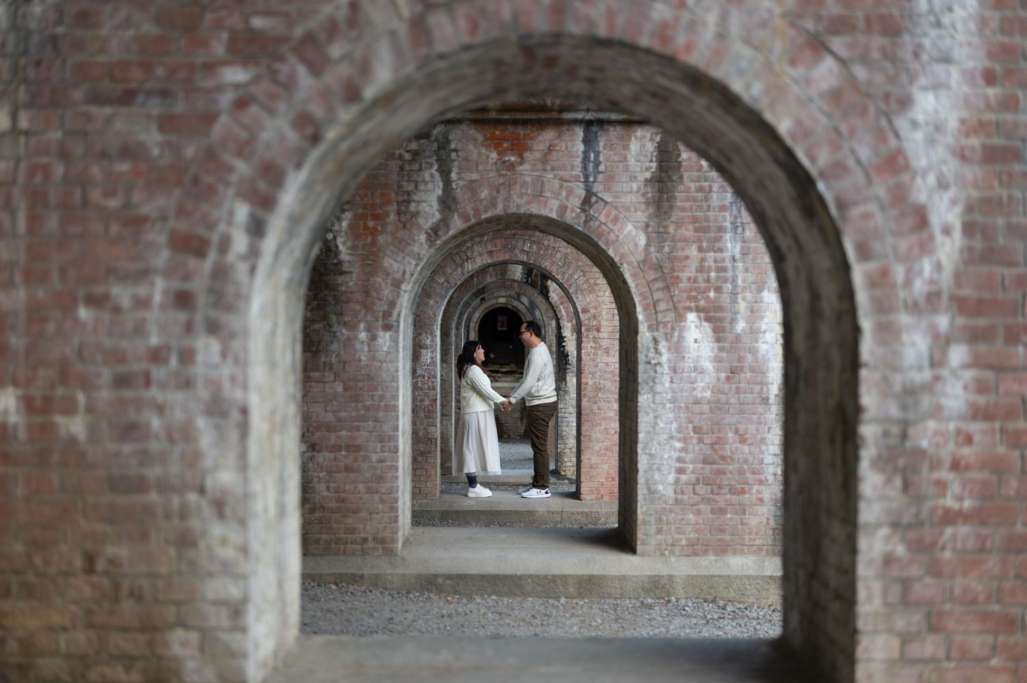 Couple sharing a romantic moment framed by a series of brick archways in a historic fort.