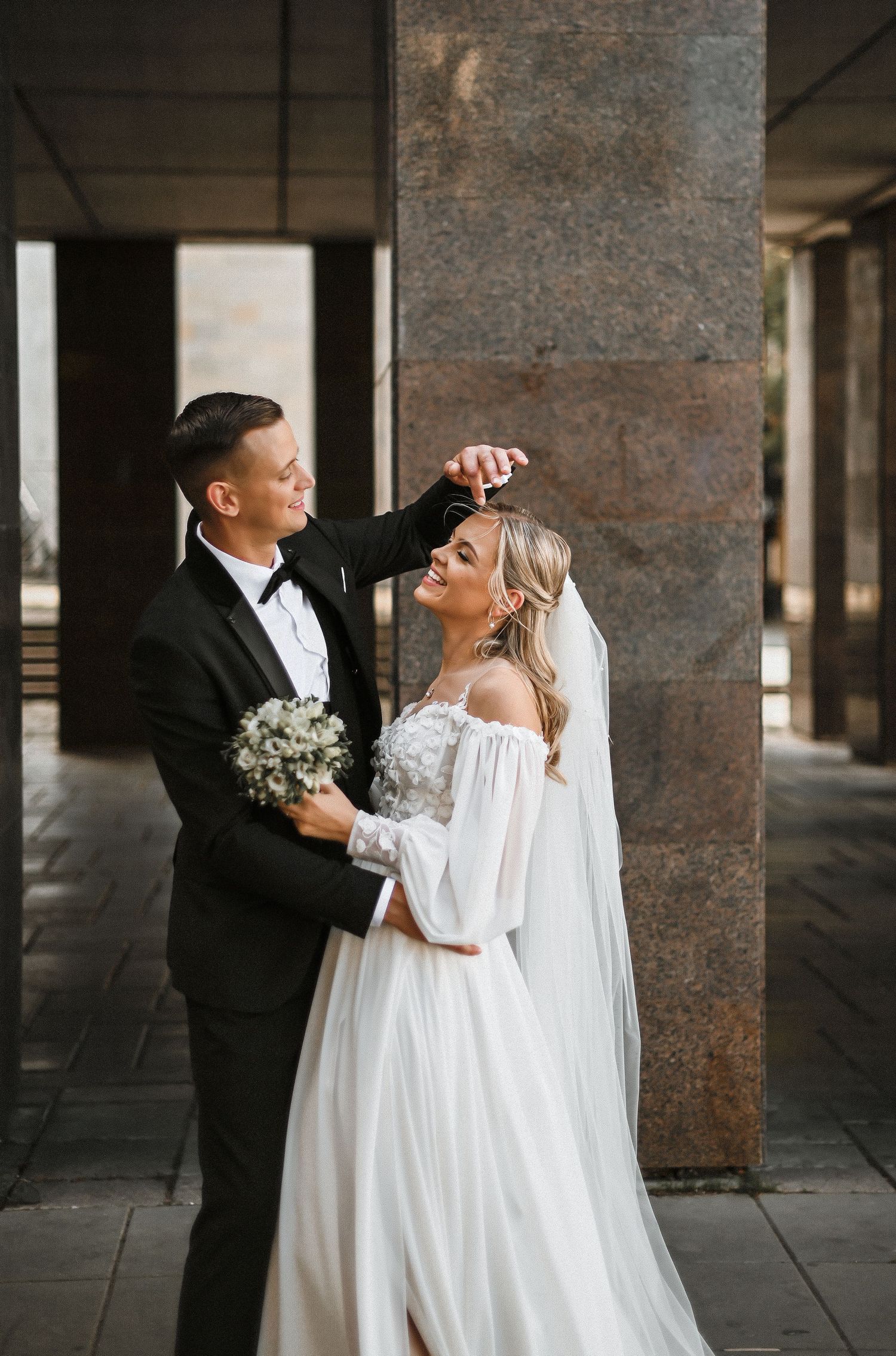 Elegant wedding couple sharing a playful moment by architectural columns.