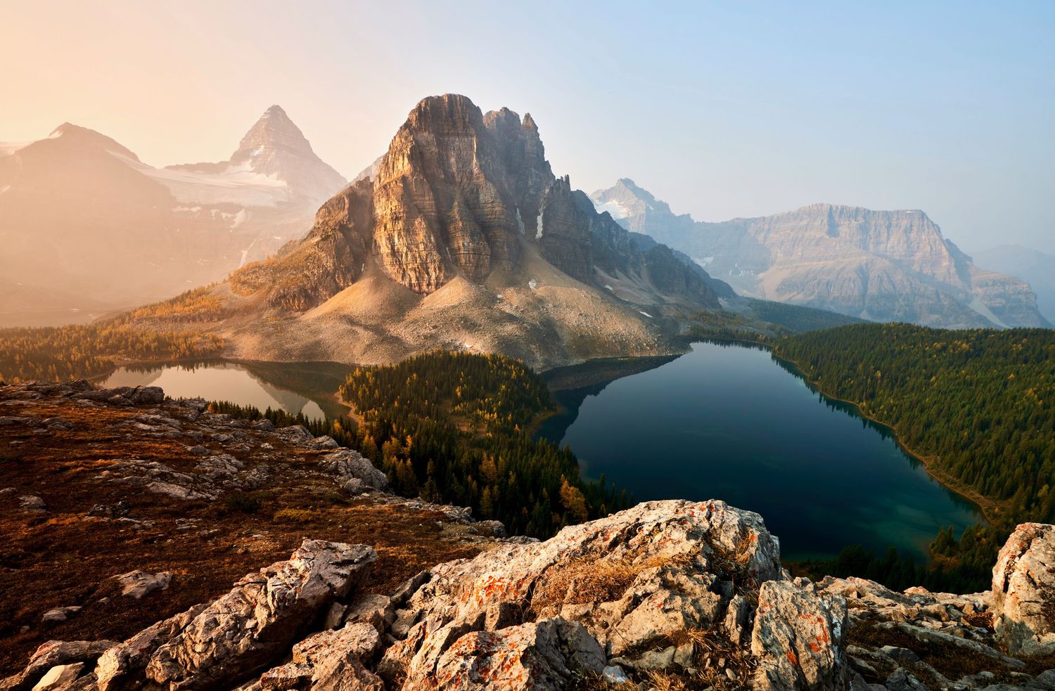 Sunlit Mount Assiniboine reflects in Sunburst Lake with dramatic rocky peaks and mountains in Banff National Park.