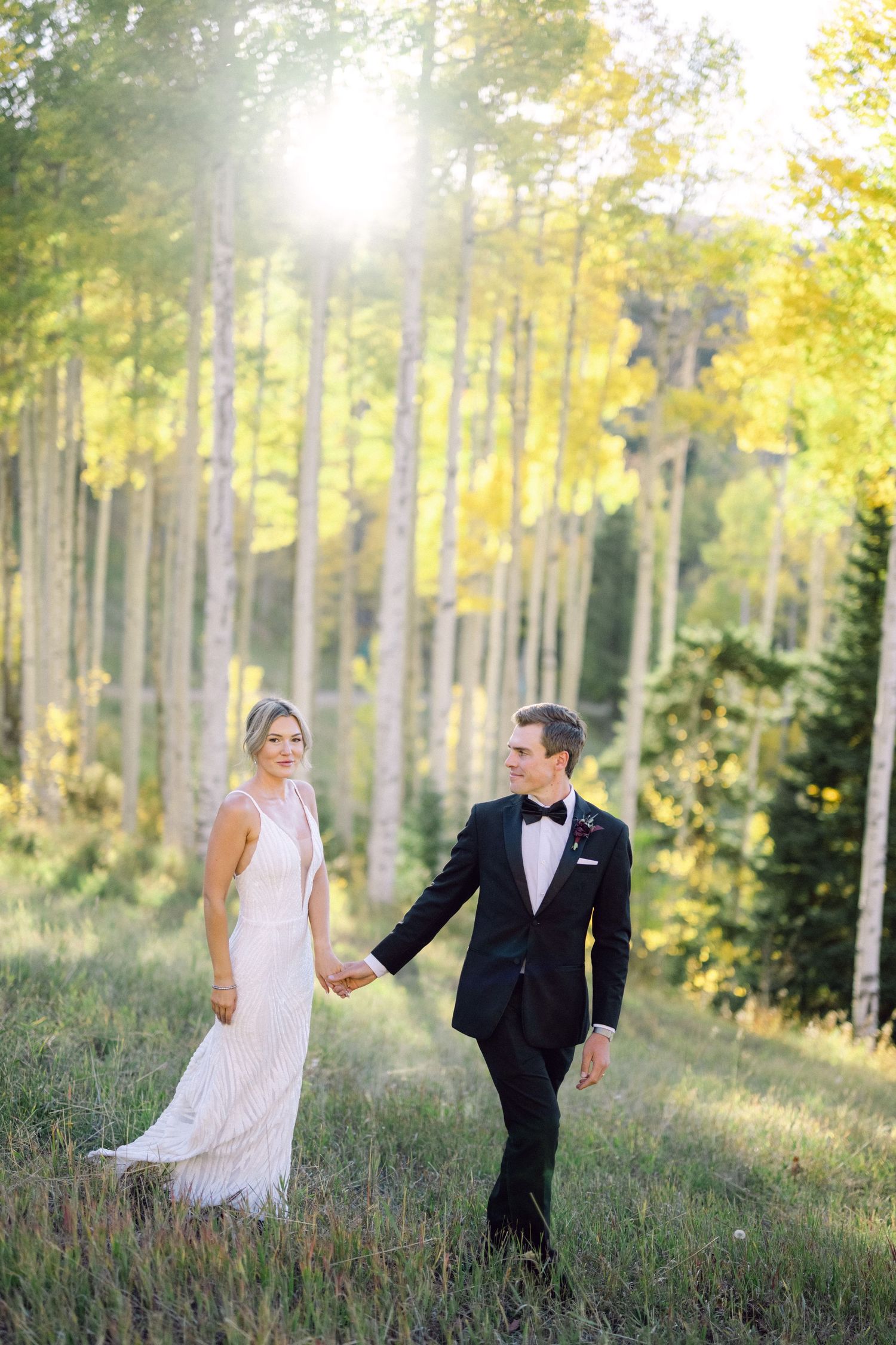 Elegant wedding couple walking hand in hand through golden aspen trees.