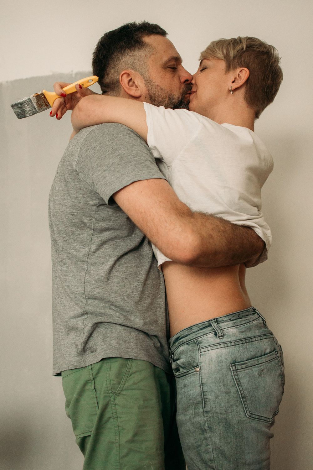 Two figures in casual clothing sharing an intimate embrace against neutral background.