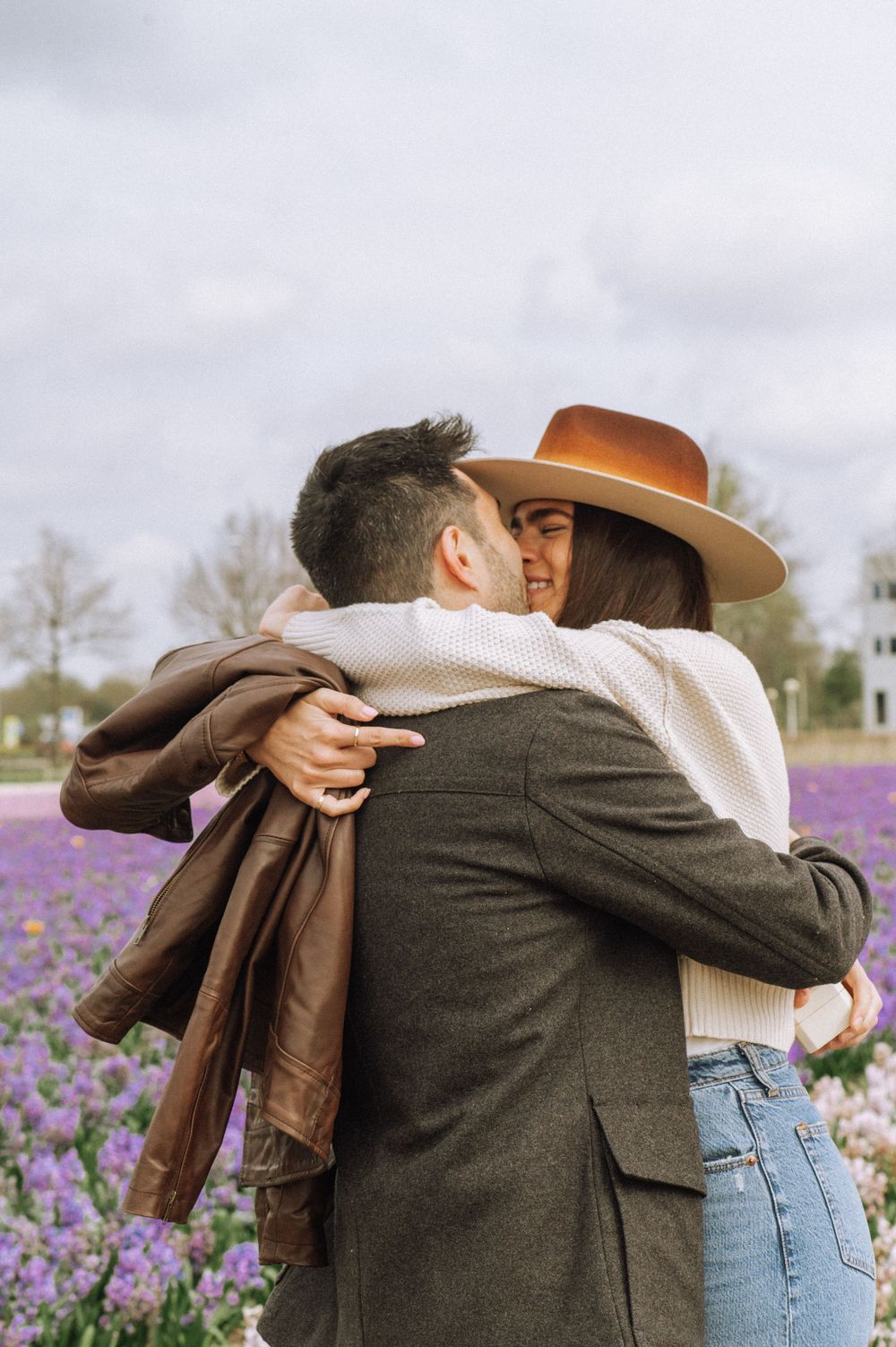 People embracing in a field of purple wildflowers with trees in the background.