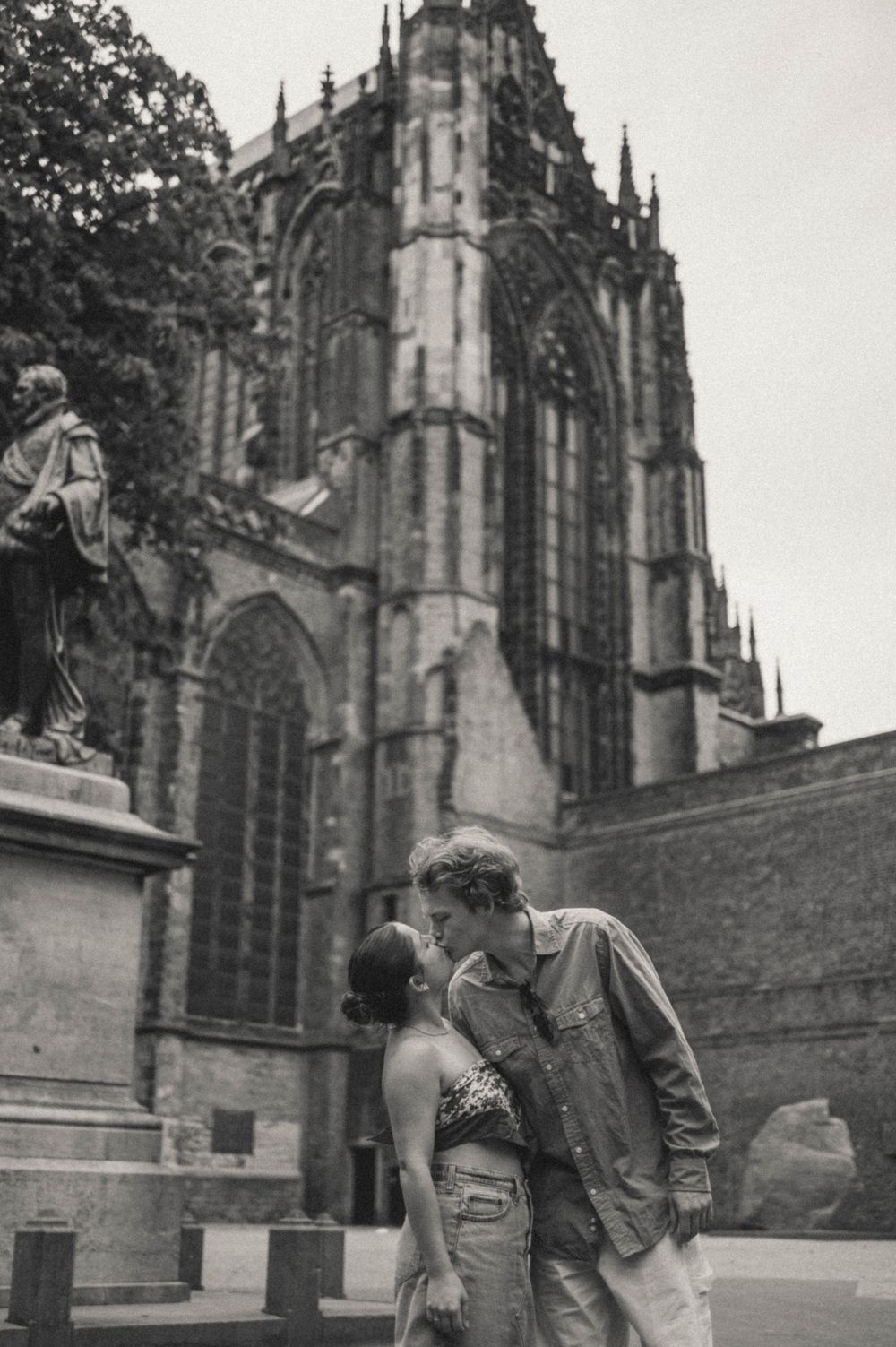 A couple shares a romantic kiss in front of a Gothic cathedral in black and white.