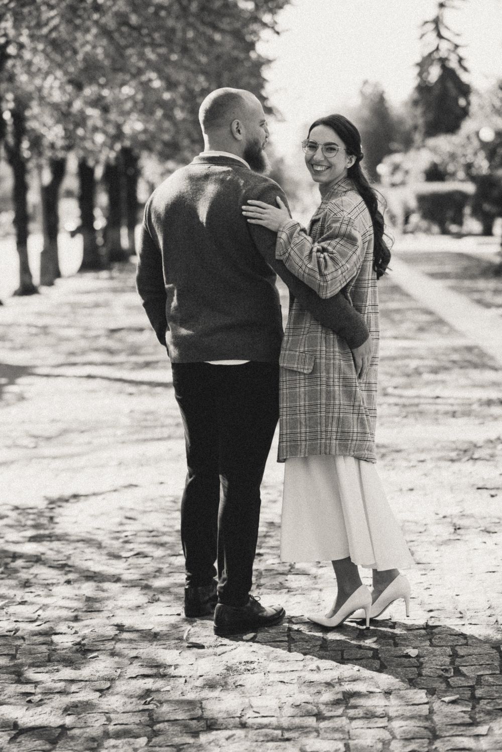 Black and white photo of a couple walking together on a cobblestone path.