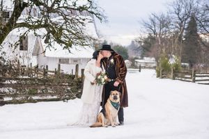 In a snowy winter wonderland, a couple pose for portraits while including their dog. January wedding at a rustic barn venue in Aldergrove BC