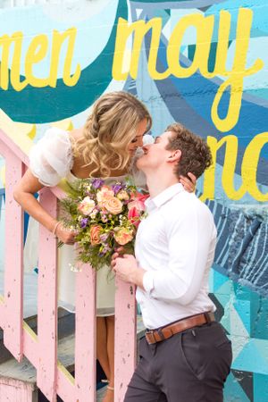 A couple playfully gazes at each other on a colourful staircase outside. Photo taken in downtown Abbotsford, BC, by Kari Mills Photography.
