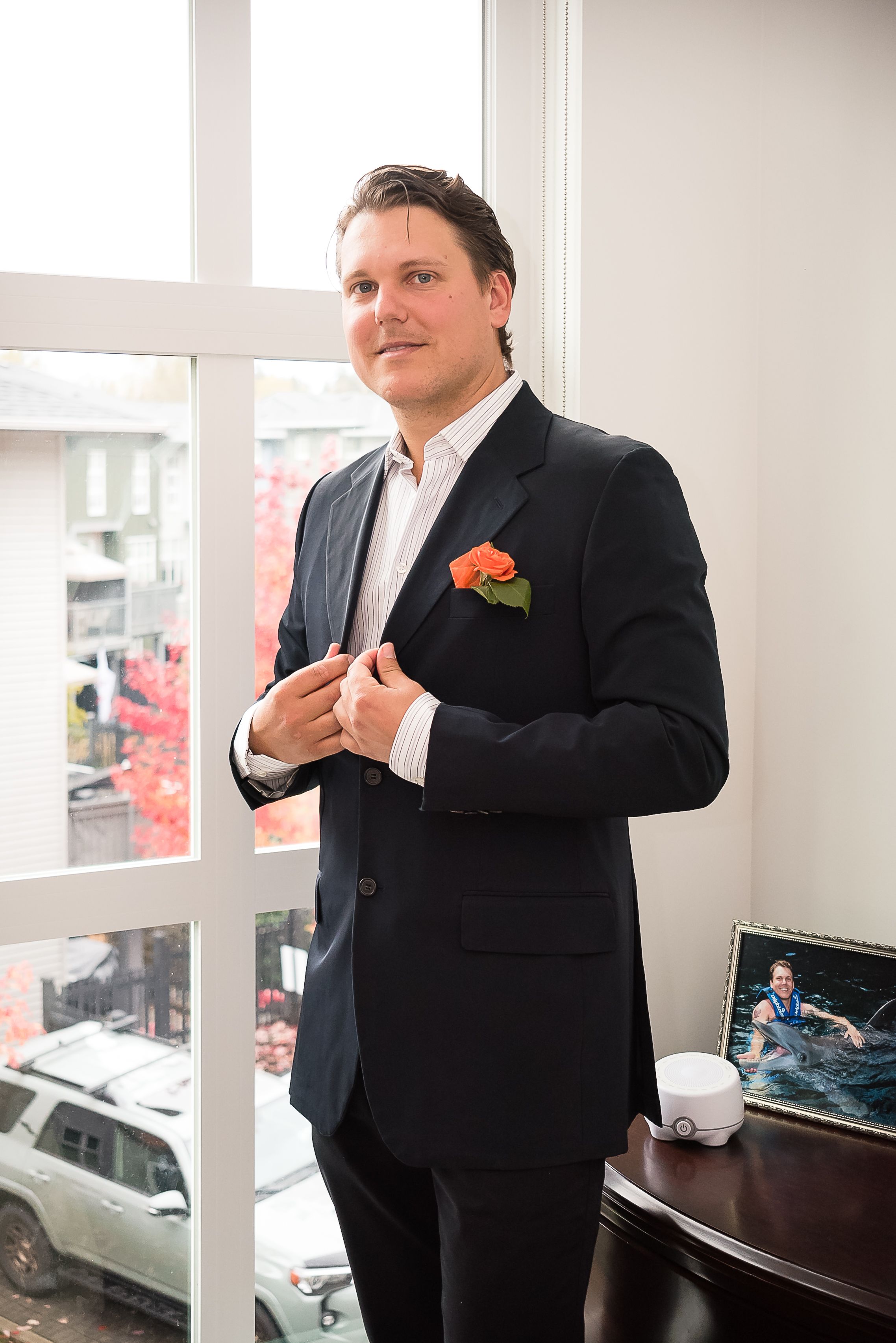 In front of a window filled with afternoon light, a groom poses stylishly for photos. An intimate at home elopement in Maple Ridge, BC.