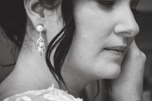 A close up black and white image of a bride putting on her earrings as she gets ready. Photo taken by Kari Mills Photography.
